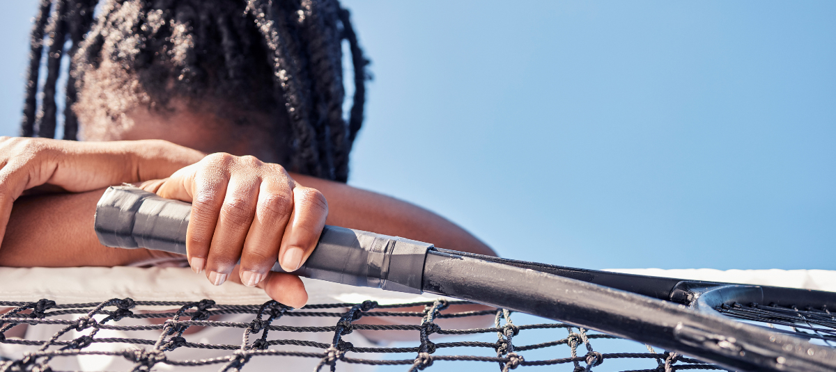 Image of a tennis player holding a racket with their head down, leaning on a net on a tennis court.