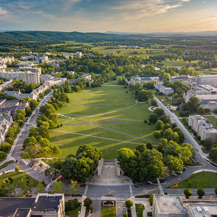 Aerial view of the Virginia Tech campus, featuring the central lawn surrounded by trees and classical architecture, with mountains in the distance.