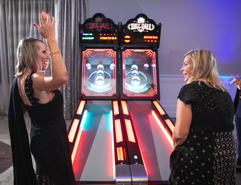 Two women in elegant clothing celebrating near two skeeball machines