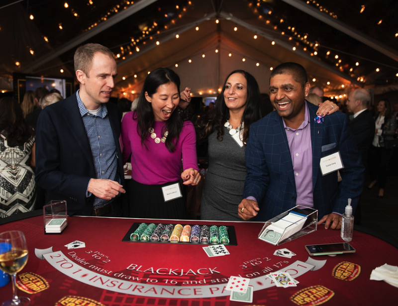 Four people standing near a blackjack table laughing